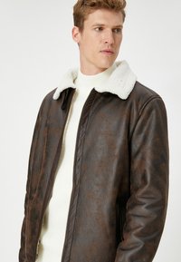 Brun faux læderjakke med en hvid shearling krave, lynlåslukning foran og sidelommer. Struktureret finish forbedrer det overordnede design.