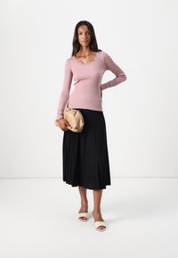 Vaaleanpunainen ribbikuvioinen pitkähihainen paita, jossa on pitsireunus, yhdistetty mustaan laskostettuun hameeseen. Asusteina vaaleanbeige laskostettu clutch-laukku ja ihonväriset liukupohjaiset sandaalit.