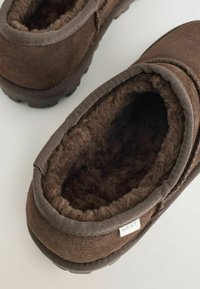 Brune ruskind slip-on sko med en blød, faux fur-foring. Har en tekstureret gummisål og et lille mærke med teksten "NEXT."