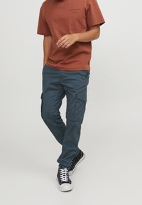 Cargo-byxor i mörkblått tyg med en jämn textur, utrustade med sidofickor och en avsmalnande passform, kombinerade med en rostfärgad t-shirt med kort ärm.