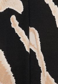 Tessuto nero con un audace motivo astratto di forme beige e crema, con dettagli testurizzati e bordi irregolari.