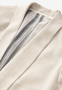 Beige cardigan met een sjaalkraag en een gestreepte voering in wit en marineblauw. Gladde textuur met zichtbare stikdetails.