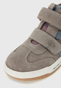 Grå suedesneaker med borrelåser, som har en teksturert overflate, hvit gummisåle, og blå og lilla detaljer på siden.