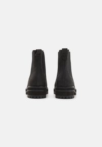 Botas negras de tobillo de ante con paneles laterales elásticos, talón reforzado y suela de goma gruesa con dibujos pronunciados.