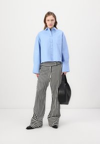 Light blue cropped shirt with buttons and pocket, paired with black and white striped wide-leg pants and carrying a black handbag.