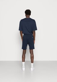 T-shirt en coton bleu marine et shorts assortis. Coupe décontractée avec des manches courtes et une poche à l'arrière des shorts. Baskets blanches et chaussettes.
