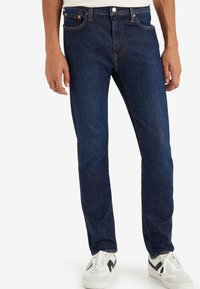 Mörkblå denimjeans med rak passform. Funktioner inkluderar framfickor, bältesöglor och knäppning med knapp. Matchas med vita sneakers.