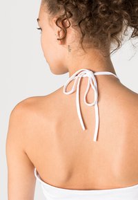 Top halter branco com fecho por laço nas costas, apresentando um design liso e justo que contorna o corpo, revelando a pele.