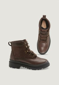 Botas de senderismo de cuero y ante marrón con suelas negras resistentes y ojales de metal, mostradas desde vistas lateral y superior sobre un fondo claro.