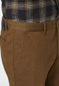 Brown cotton trousers with a smooth texture, featuring front pockets, a belt loop, and a leather brand patch on the back waistband.