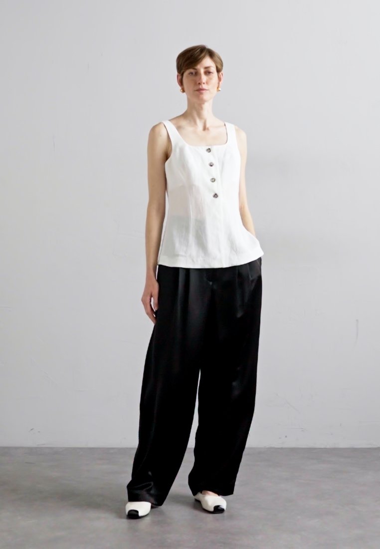 Haut sans manches blanc avec décolleté carré et détails de boutons, associé à un pantalon noir ample. Textures lisses et silhouette surdimensionnée.