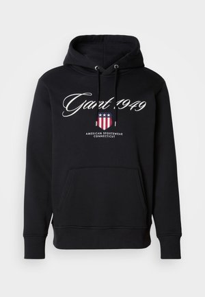Fekete kapucnis pulóver fehér "Gant 1949" felirattal, pajzs logó csillagokkal és csíkokkal, valamint "American Sportswear Connecticut" szöveggel, elülső kenguru zsebbel.