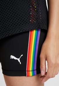 Mustat urheilushortsit, joissa on valkoinen Puma-logo ja kirkas sateenkaaristripti sivussa. Verkkomateriaalia oleva toppi, jossa on pyöreitä aukkoja päällä.