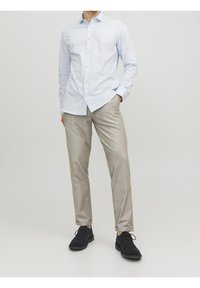 Světle modrá košile na knoflíky s dlouhými rukávy, kombinovaná s béžovými slim-fit kalhotami a tmavými botami. Tkaniny vypadají hladce a dobře padnou.