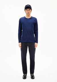 Camisa de manga larga navy con escote en crew, combinada con jeans de mezclilla azul oscuro y zapatos negros. Diseño simple, textura suave.