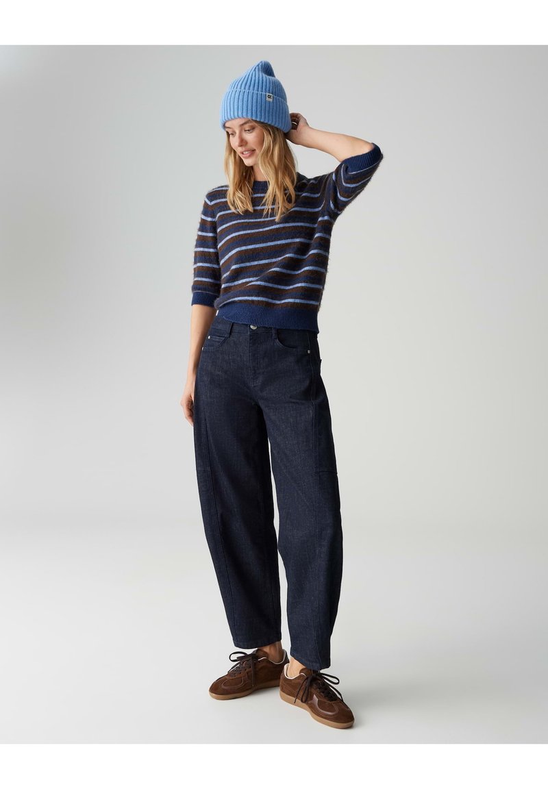 Pull à rayures bleues tricoté à manches courtes, associé à un pantalon large bleu foncé et des baskets marron. Bonnet bleu sur la tête.