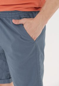 Herrblå shorts tillverkade av lättviktig tyg, med en sidficka, elastisk midja och slät yta.