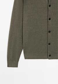 Cardigan vert olive à manches longues boutonné avec poignets et ourlet côtelés, présenté de la moitié de la manche jusqu'à la taille sur fond blanc.