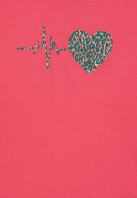T-shirt corail avec un design en forme de cœur imprimé léopard intégré à une ligne de battement de cœur en vert et noir. Texture de tissu douce.