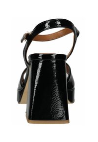 Czarne lakierowane sandały na słupku z paskiem wokół kostki, gładka tekstura, otwarte z tyłu, z beżowym skórzanym wykończeniem. Posiadają szeroki obcas dla większej stabilności.