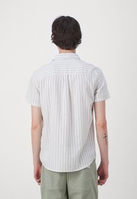 Korte mouwen blouse van lichte stof met verticale blauw-witte strepen, met een puntige kraag en een rechte achterkraag.