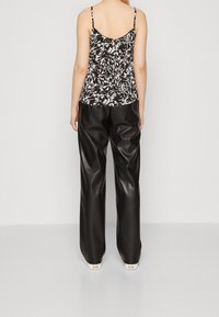 Zwart-wit bloemenpatroon cami-top met dunne bandjes, gecombineerd met hoge taille zwarte nep leren wijde broek.