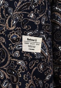 Țesătură de catifea corpolentă în nuanțe de bleumarin, cu un model paisley în tonuri de bej, albastru și marron. Prezintă o etichetă albă cu text negru care detaliază marca și scopul.