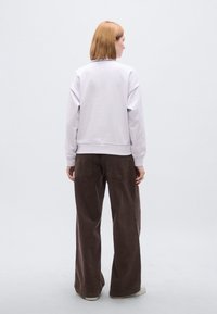 Μαλακό μοβ φούτερ με ριμπ μανσέτες, συνδυασμένο με φαρδιά καφέ σκούρα παντελόνια. Το σύνολο έχει μινιμαλιστικό σχεδιασμό και άνετη, καθημερινή σιλουέτα.