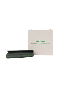 Portafoglio in pelle verde con design pieghevole, caratterizzato da una superficie liscia e una chiusura con cinturino, accanto a una scatola beige etichettata "Maitre Finest Leathergoods."