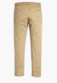 Chinos beige avec une coupe droite, dotés de deux poches arrière à fermeture par bouton et de détails cousus le long des coutures.