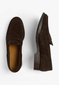 Mocasines de ante marrón con un detalle de costura elevada y un tacón plano de madera. Presentan un forro de cuero suave y punta redondeada.