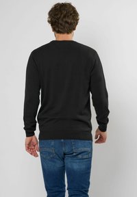 Schwarzer Strickpullover mit langen Ärmeln, Rundhalsausschnitt und gerippten Bündchen, kombiniert mit blauen Jeans. Einheitliche Textur, ohne sichtbare Muster.