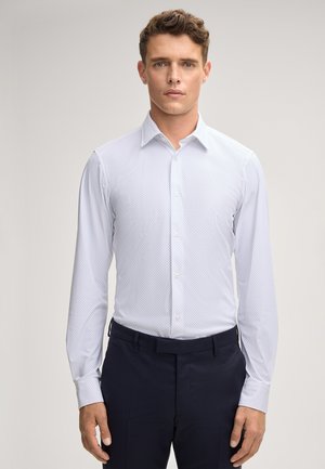 Camicia azzurro chiaro con un delicato motivo a pois, maniche lunghe e colletto a punta, abbinata a pantaloni scuri. Chiusura frontale con bottoni.