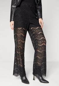 Zwarte kant palazzo-broeken met geschulpte randen en een doorzichtig ontwerp, gedragen met zwarte enkellaarsjes met hak. Geweven stof met ingewikkelde patronen.