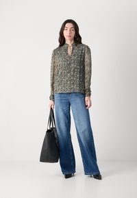 Bluză cu imprimeu floral, cu guler înalt și închidere cu fundă, asociată cu blugi largi de culoare albastră și o geantă mare neagră. Texturi netede pe tot parcursul.
