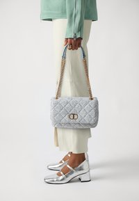 Quilted light blue handbag with gold hardware, chain straps, and a flap closure. Accessories are silver block-heeled shoes, textured and shiny.