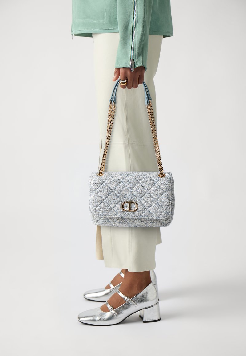 Quilted light blue handbag with gold hardware, chain straps, and a flap closure. Accessories are silver block-heeled shoes, textured and shiny.