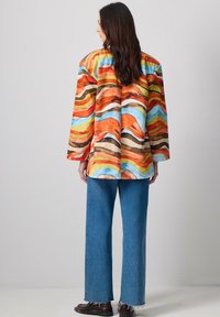 Colorful oversized jacket with abstract wave pattern in orange, blue, and yellow; paired with loose blue denim jeans and dark shoes.