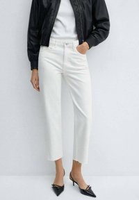 Vaqueros blancos recortados con dobladillo deshilachado, confeccionados en denim, combinados con una camiseta blanca ajustada y una chaqueta bomber negra. Tacones negros de punta afilada.