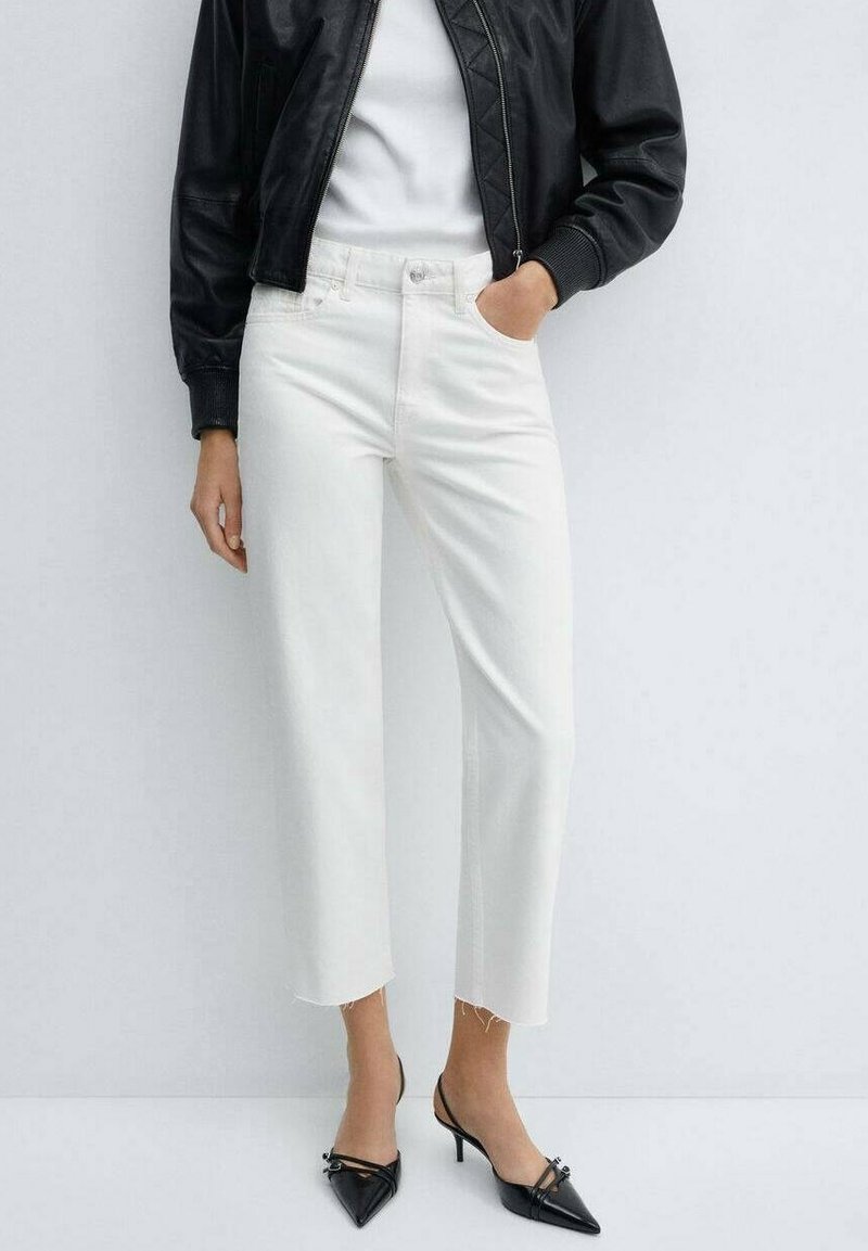 Vaqueros blancos recortados con dobladillo deshilachado, confeccionados en denim, combinados con una camiseta blanca ajustada y una chaqueta bomber negra. Tacones negros de punta afilada.