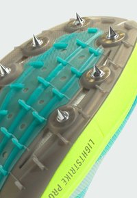 Klart gul och turkos atletisk skosula med spikar, texturerad design, klara plastdetaljer och ingraverad märkning på sidan.