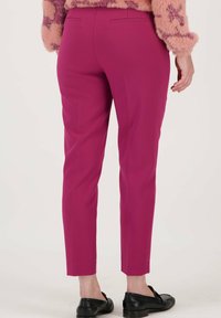 Pantalons ajustés, longueur cheville, en tissu rose vif avec une texture lisse et deux poches arrière, associés à des chaussures noires à enfiler.