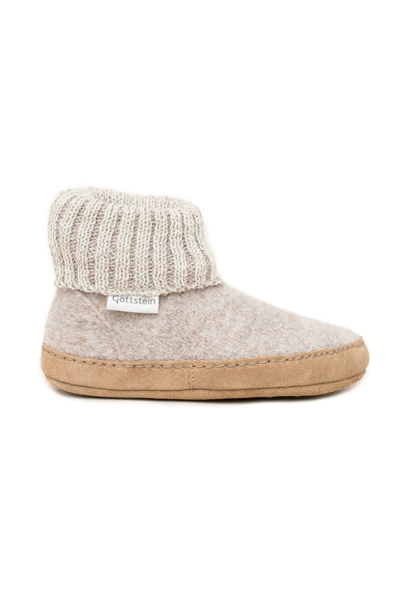 Pantofola in morbida lana beige con suola in suede marrone e bordo a costine, caratterizzata da una piccola etichetta bianca sul lato.