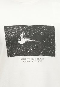 Αστροναύτης που ιππεύει έναν κομήτη μέσα σε έναν ουρανό γεμάτο αστέρια με το κείμενο «Ride Your Dreams Carhartt WIP» από κάτω.