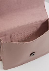 Portafoglio in pelle mauve chiaro aperto, con scomparti per carte cuciti e chiusura con bottone magnetico su una superficie bianca.