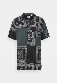 Camicetta nera e grigia a maniche corte con motivi bandana, caratterizzata da un colletto e bottoni. Realizzata in tessuto leggero.