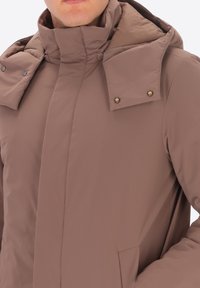 Giacca isolante marrone con colletto alto, bottoni a scatto e tasche laterali. Texture liscia e design aderente, adatta per il freddo.