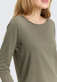 Olijfgroen shirt met lange mouwen en een ronde hals, gemaakt van zachte stof; heeft een gladde textuur en een eenvoudig ontwerp zonder patronen.