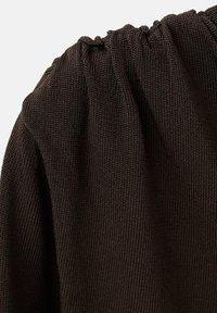 Tejido de punto marrón con un detalle de escote fruncido. La textura es suave con un patrón de tejido fino, mostrando un ligero brillo bajo la luz.