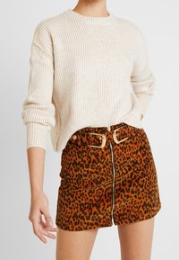 Sweter z dzianiny w paski w odcieniach beżu i kremu, połączony z pomarańczową spódnicą z kordurowego materiału z nadrukiem w panterkę i podwójnym zapięciem na złote klamry.